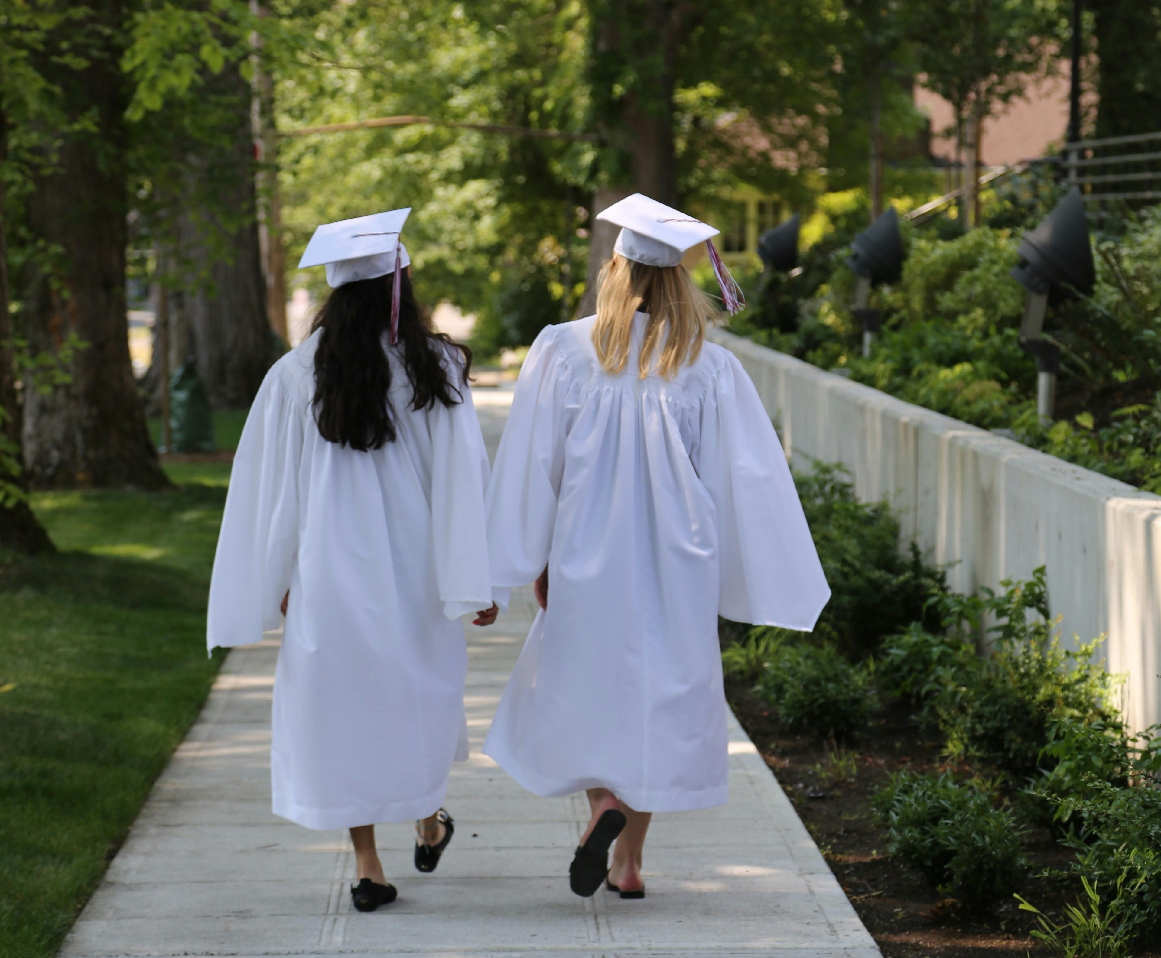 Two people in graduation gowns and caps walking away