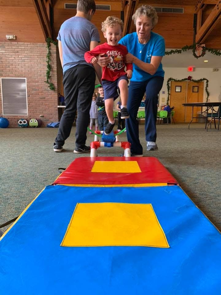 Adults helping a child jump over an obstacle on a mat
