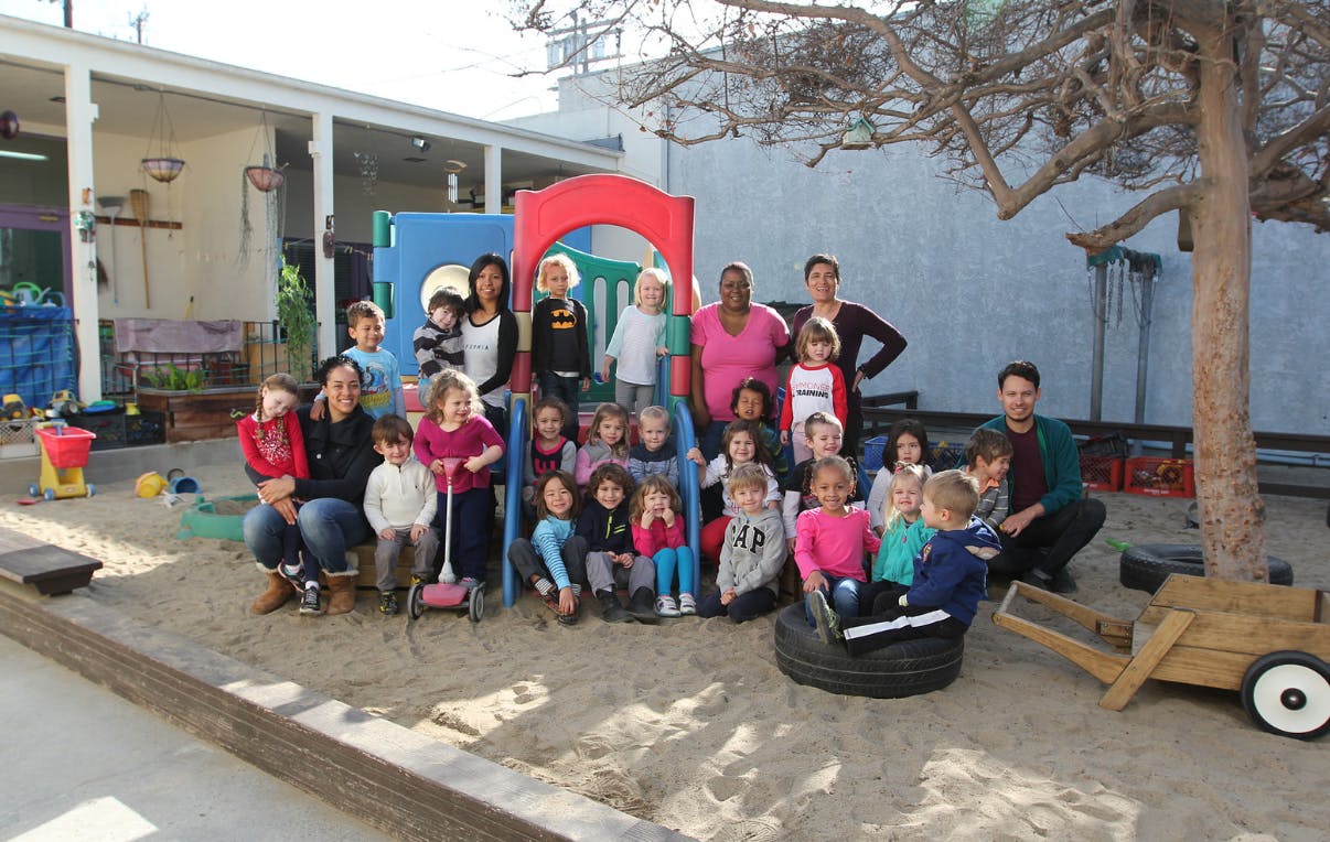 Group of adults and children posing in a sandbox with playground equipment