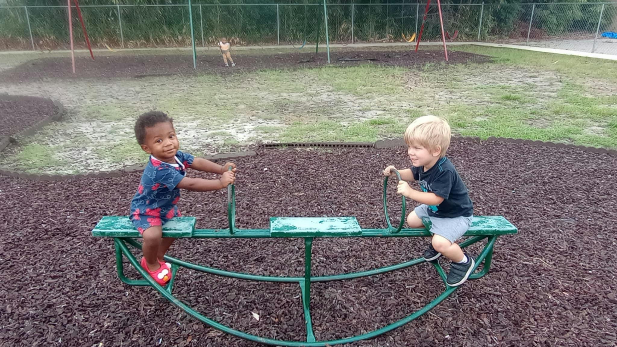 Two children on a green seesaw at a playground