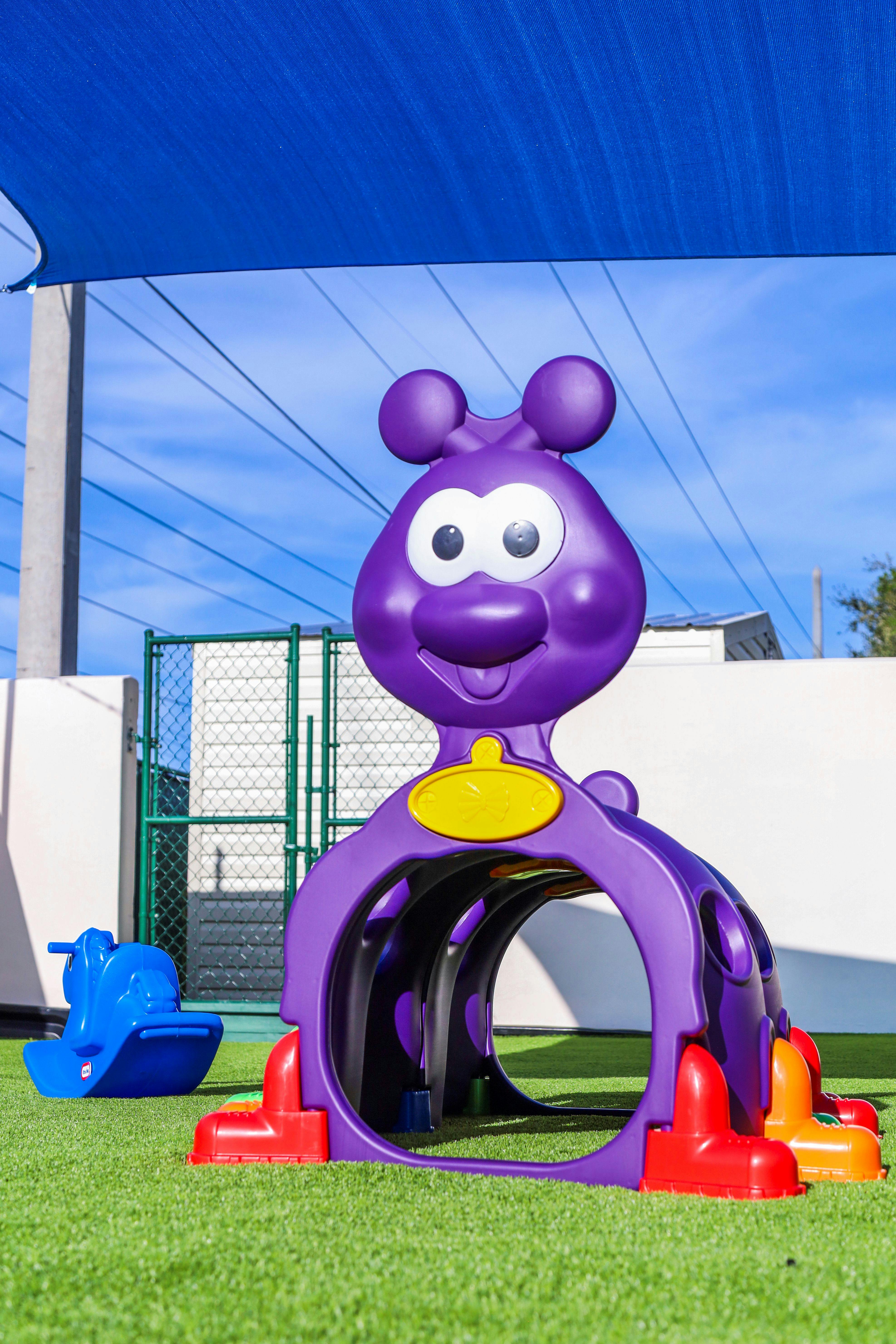 Purple caterpillar play tunnel and blue rocking toy on artificial grass