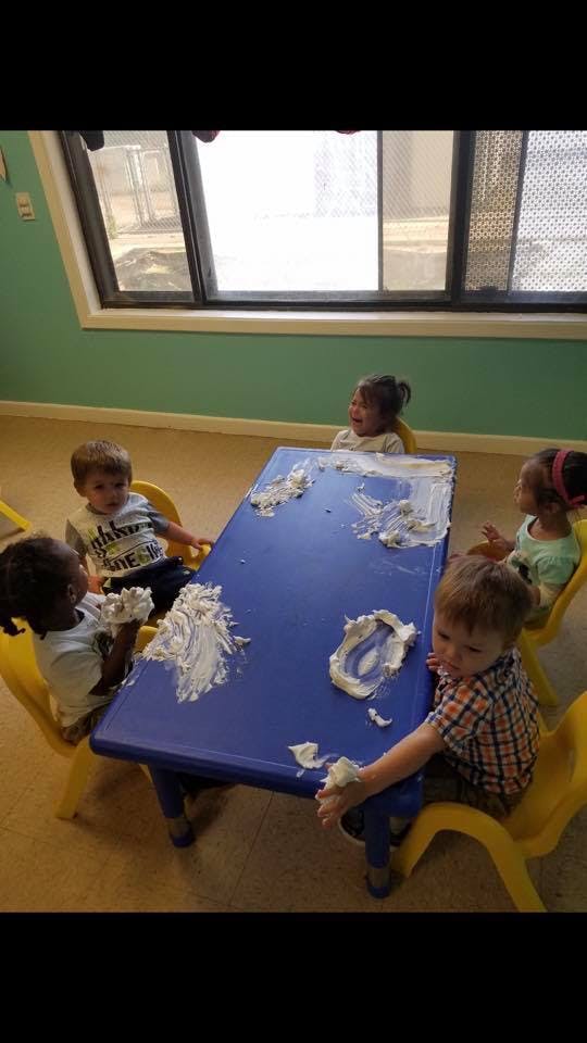 Children playing with white foam on a blue table in a classroom