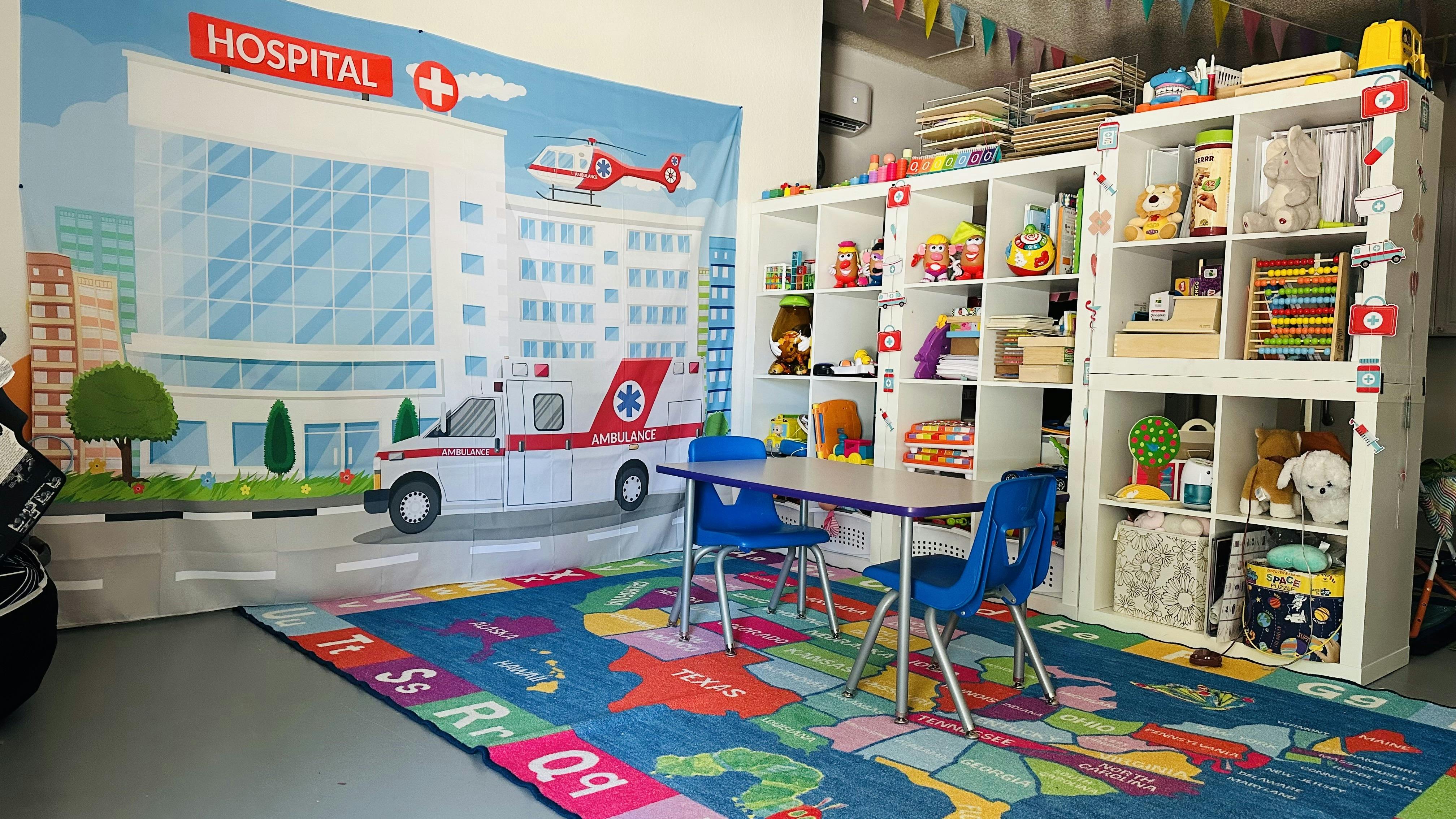 Playroom with hospital mural, table, chairs, and shelves with toys