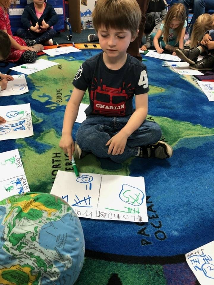 Child drawing on paper on a map rug in a classroom