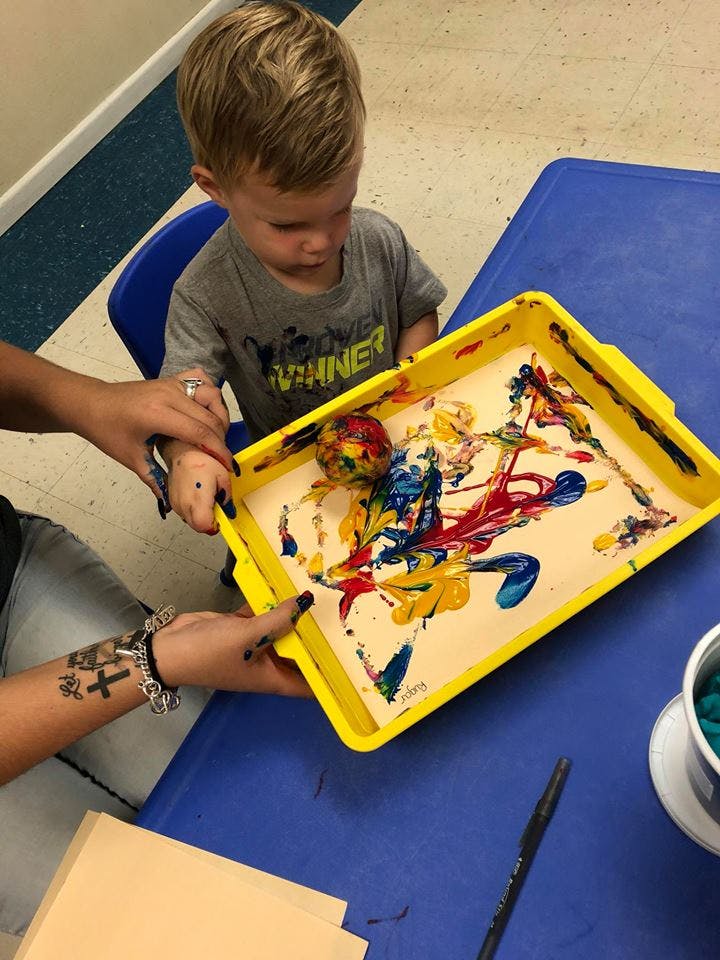 Child and person doing a paint activity with a ball in a yellow tray