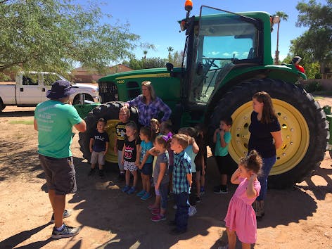 Adults and children gathered around a large green tractor