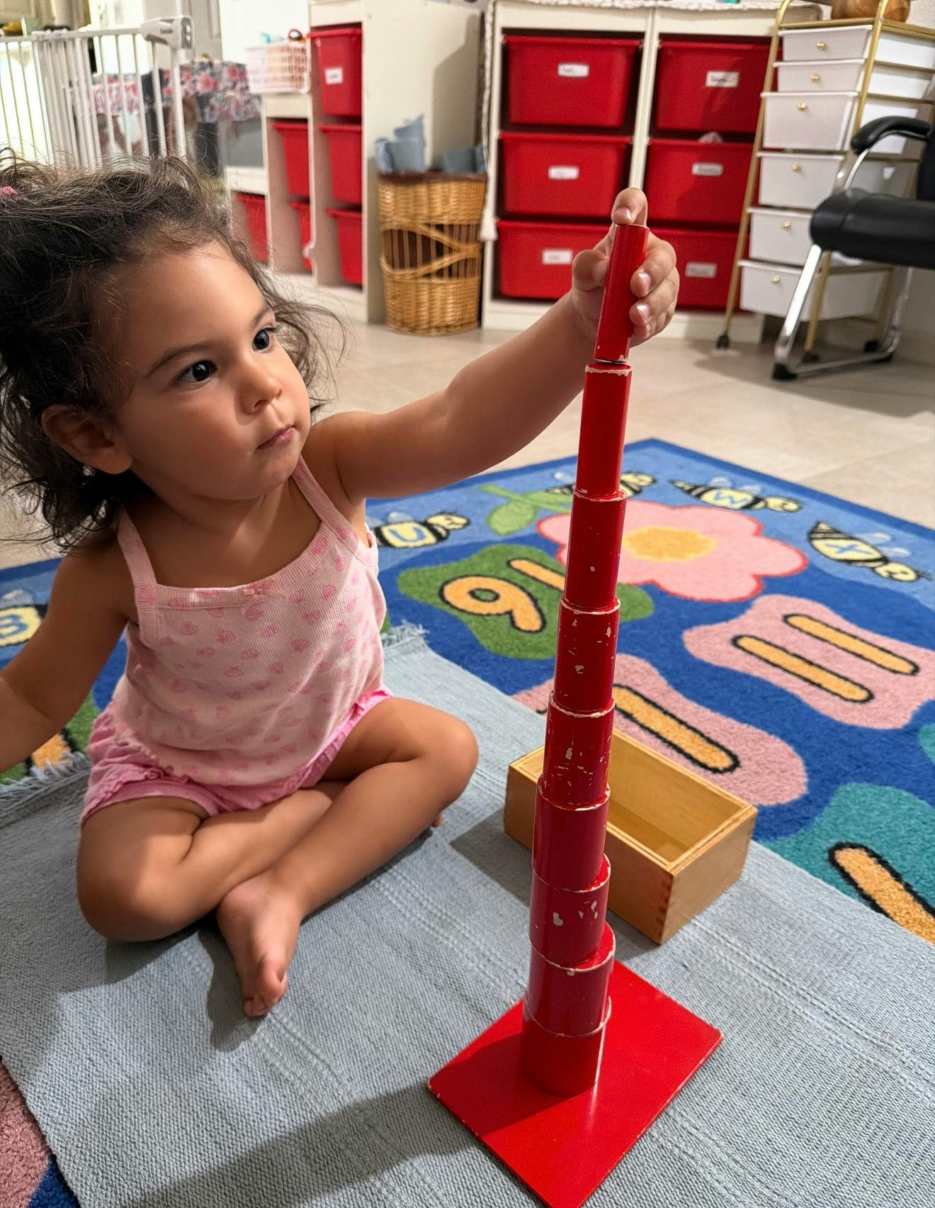 Child stacking red cylinders on a base