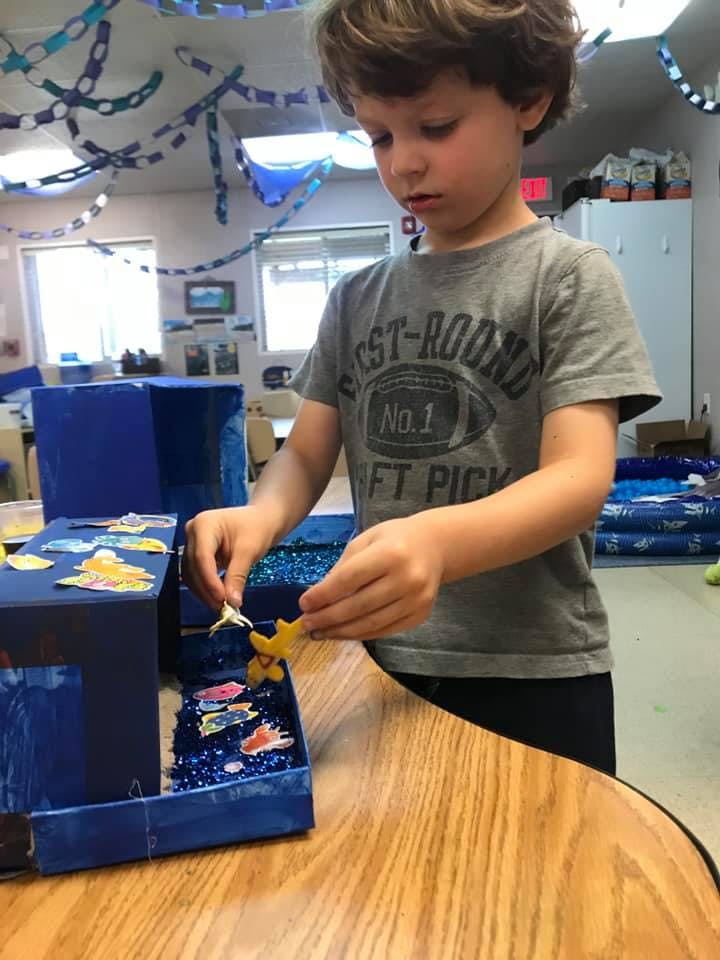 Child placing a cutout into a blue box with other cutouts