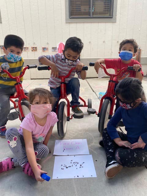 Children in face masks on tricycles and sitting on the ground