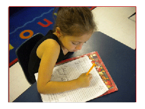 Child writing on paper with a pencil at a desk
