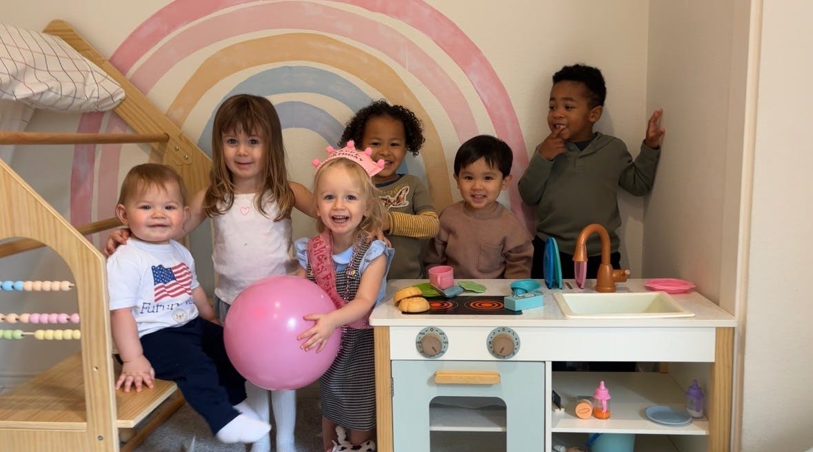 Group of children playing in a room with a play kitchen and wooden climbing toy