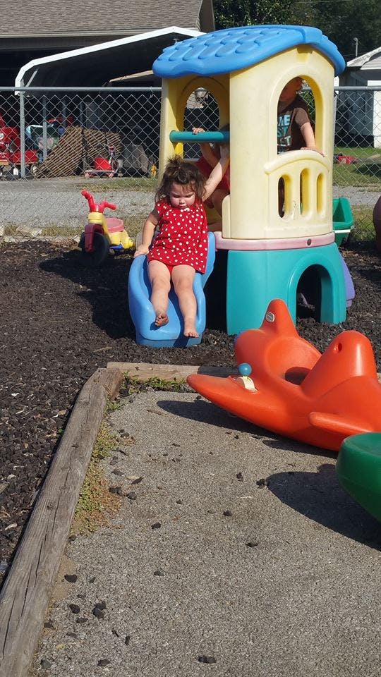 Child in a red polka dot dress sitting on a blue slide on a playground