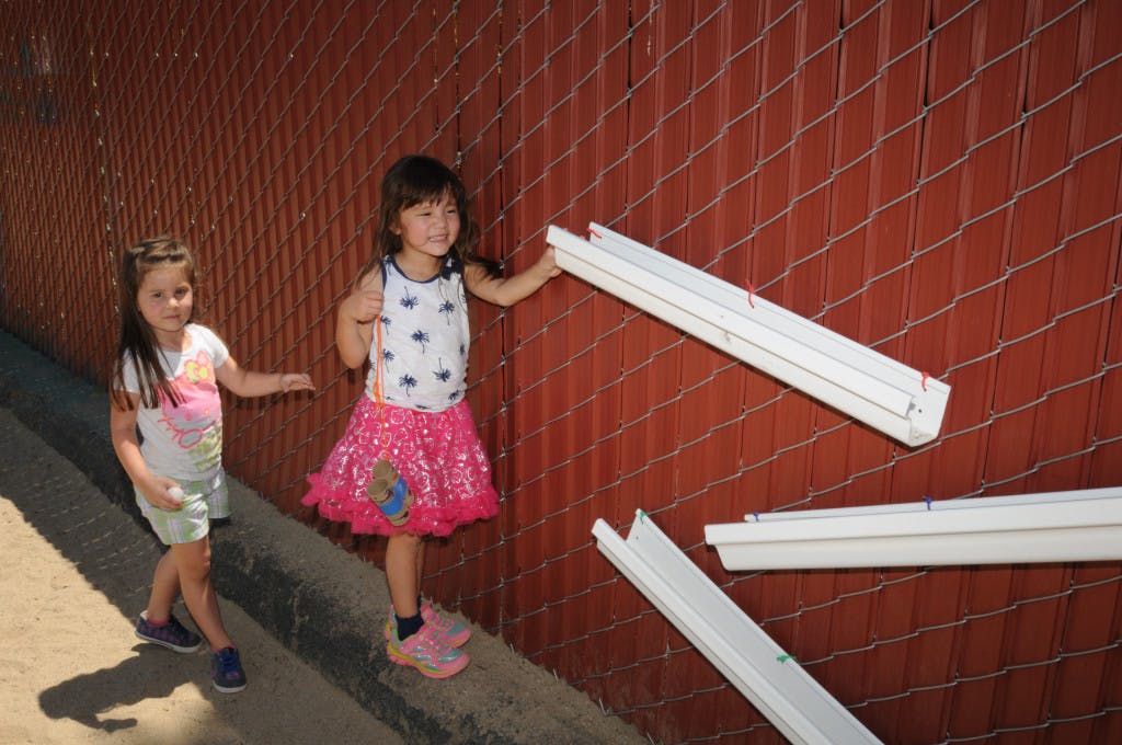 Two children standing by a red fence, one holding a white object
