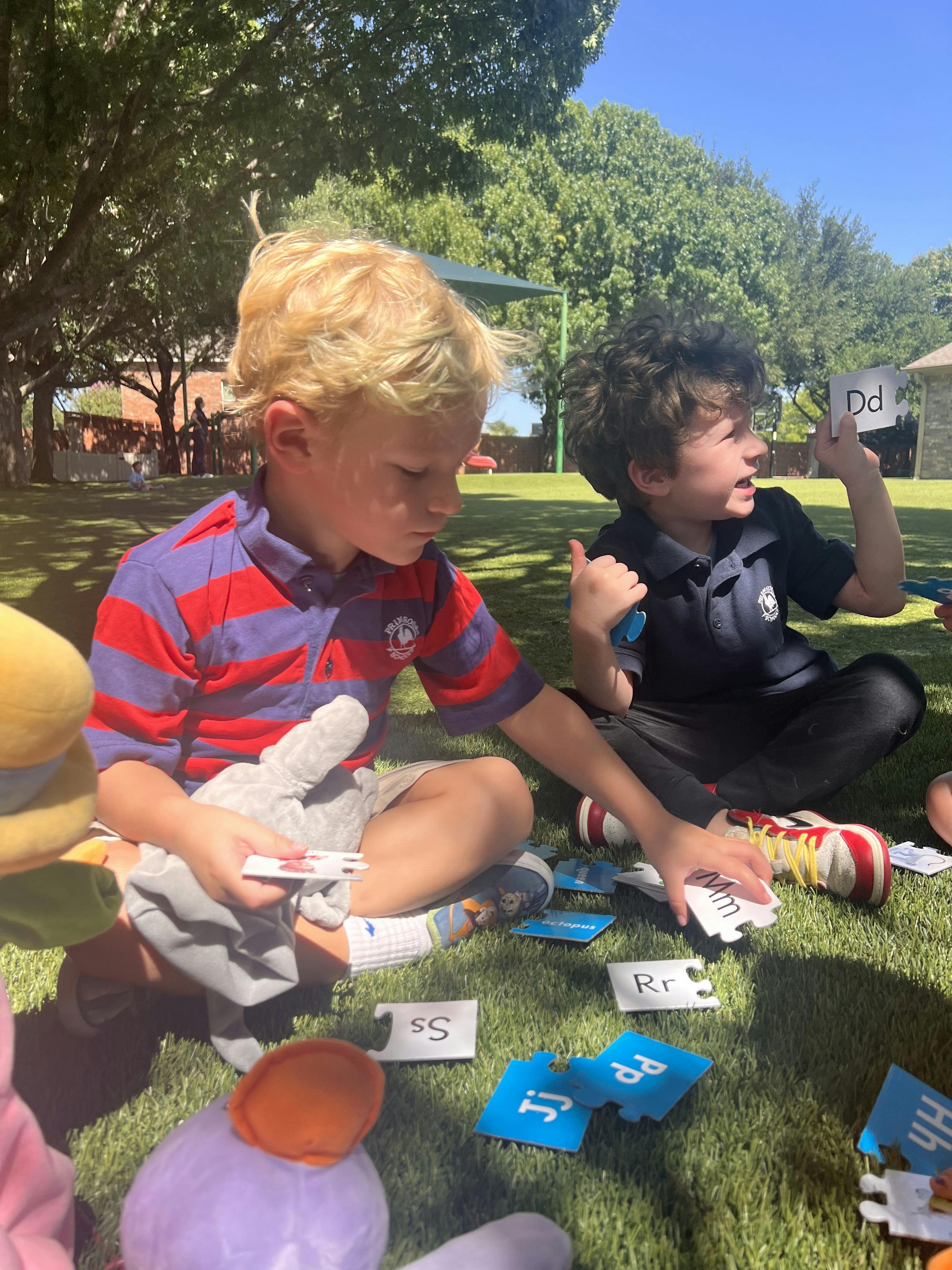 Two children sitting on the grass playing with letter puzzle pieces