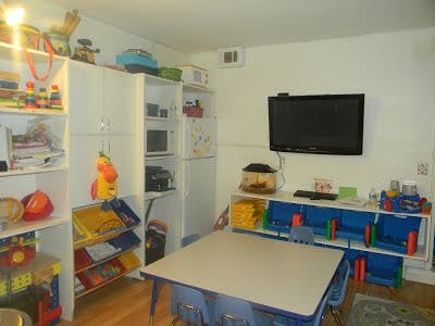Classroom with shelves of toys, a table with chairs, and a wall-mounted TV