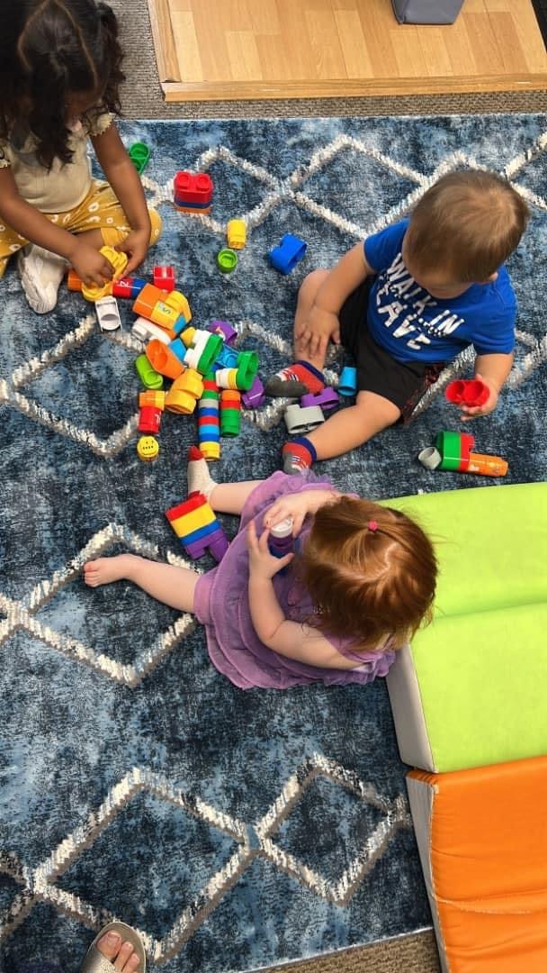 Three children playing with colorful building blocks on a rug
