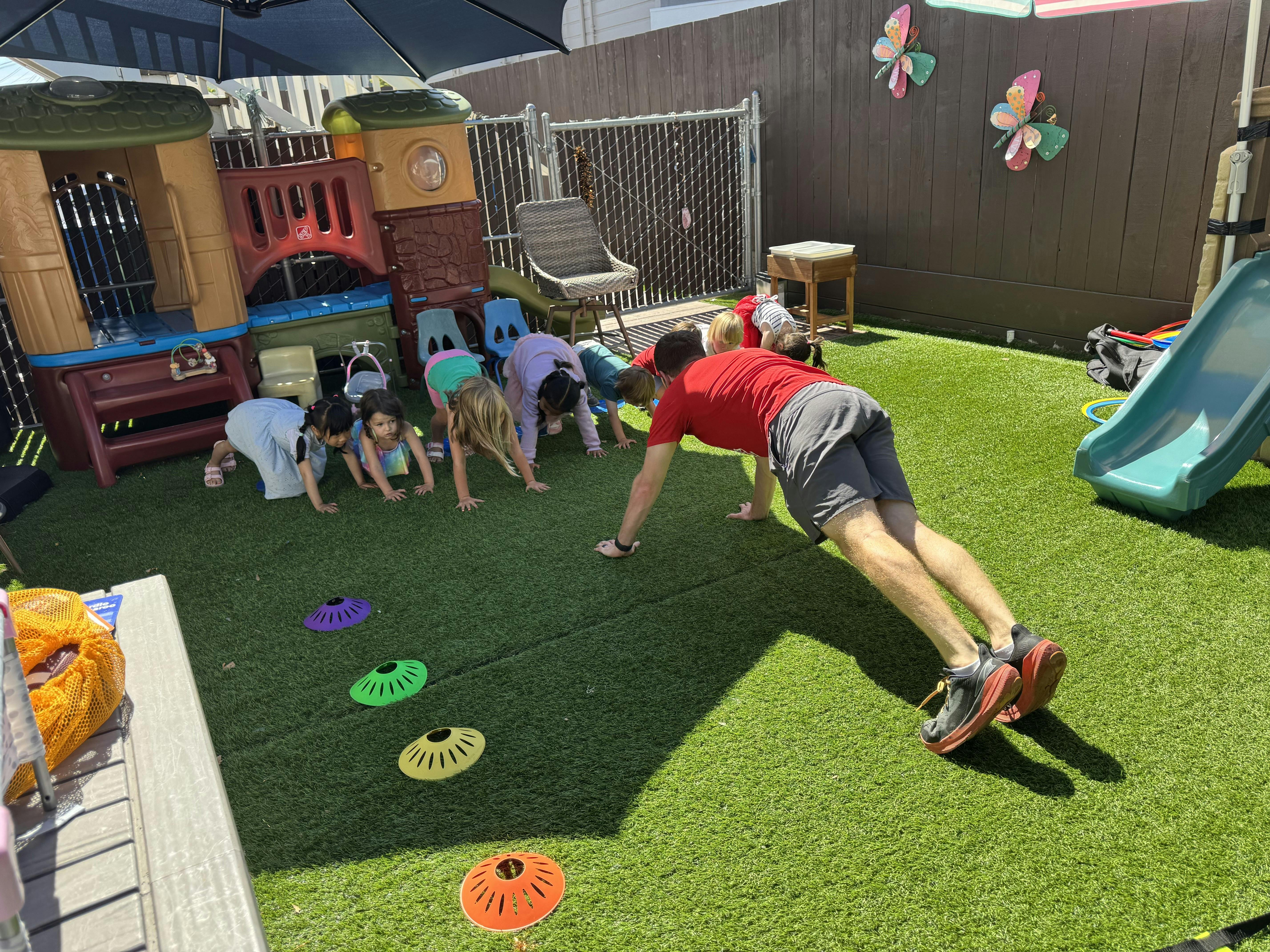 A man and several children in a plank position on a green artificial turf playground