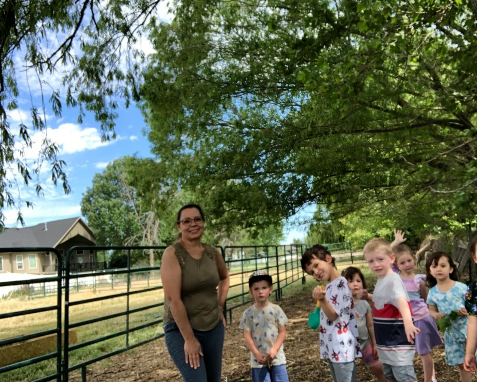 Adult and group of children standing outdoors near a fence