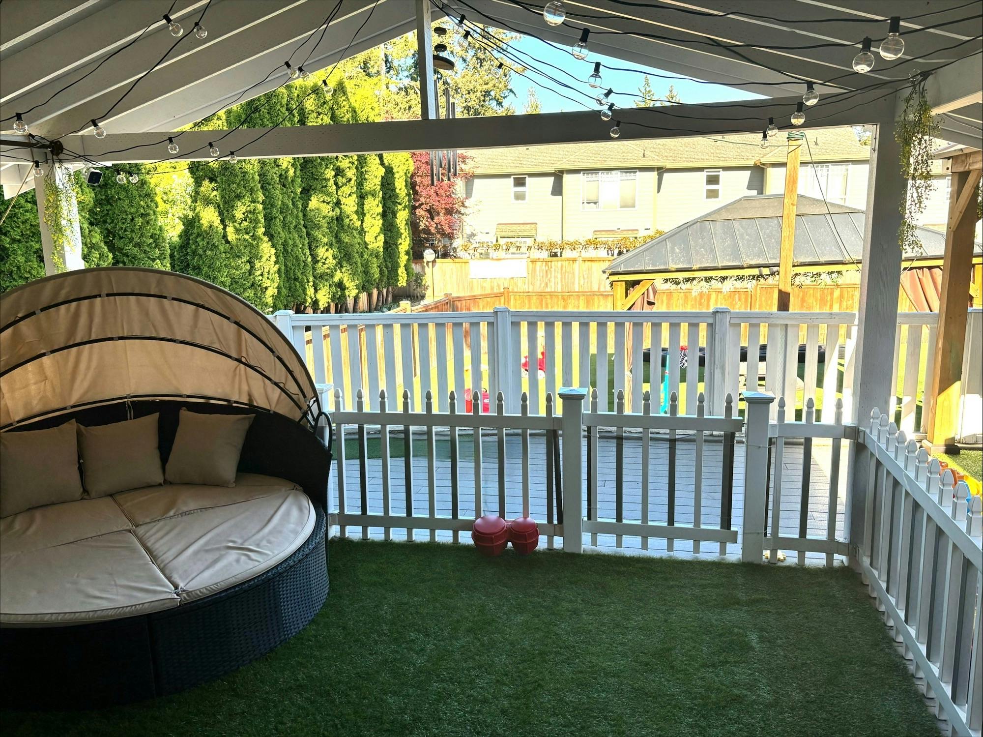 Outdoor daybed under a covered patio next to a white fence
