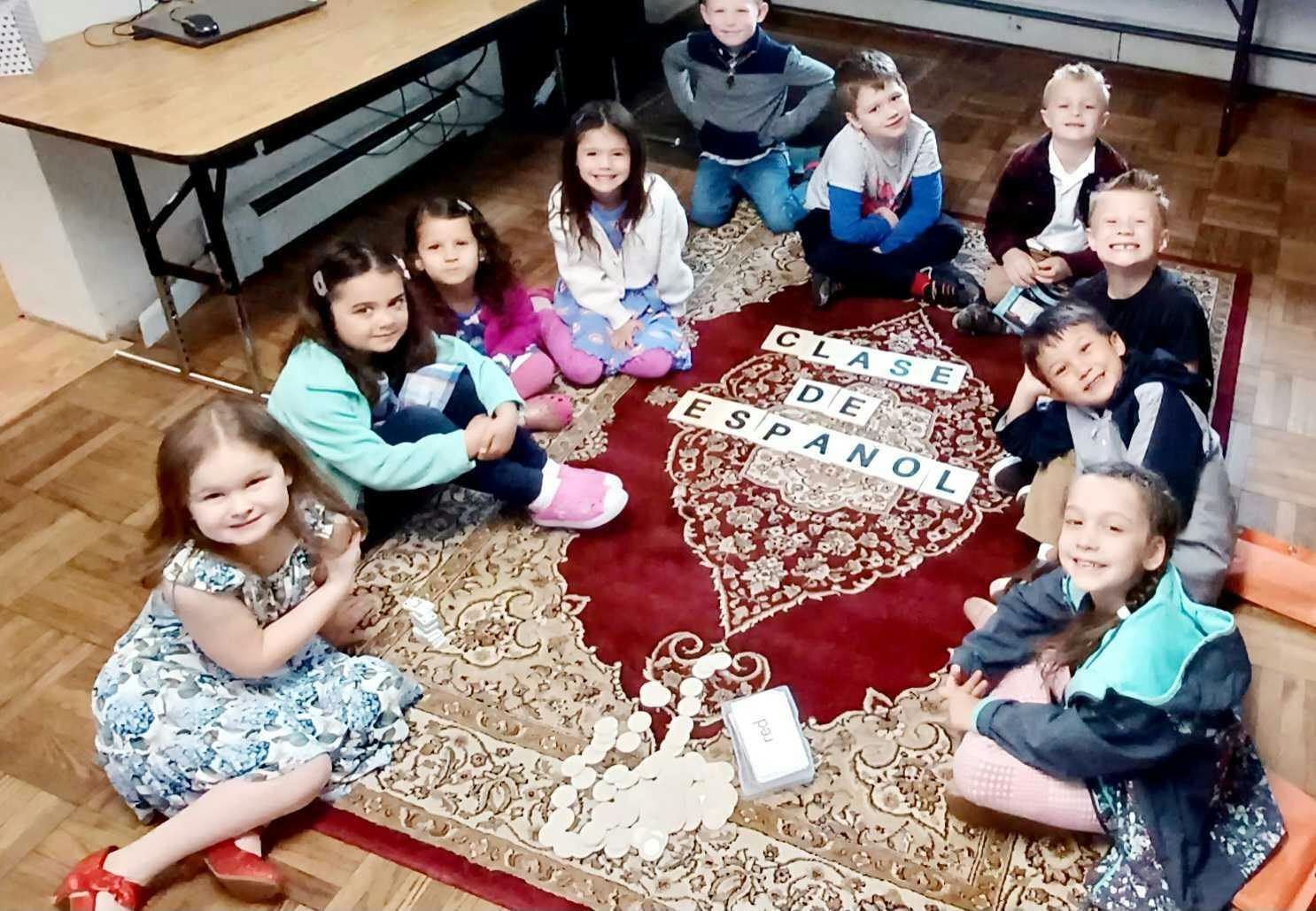 Group of children sitting on a rug labeled Clase de Español in a classroom