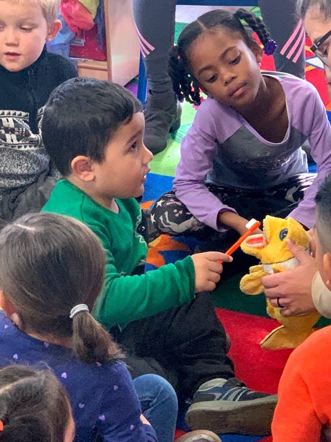 Child holding a toothbrush to a stuffed animal's mouth in a classroom