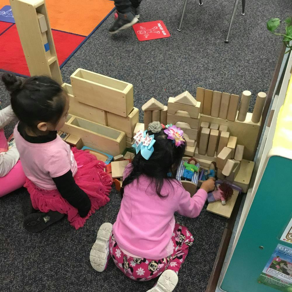 Two children playing with wooden blocks on a carpeted floor