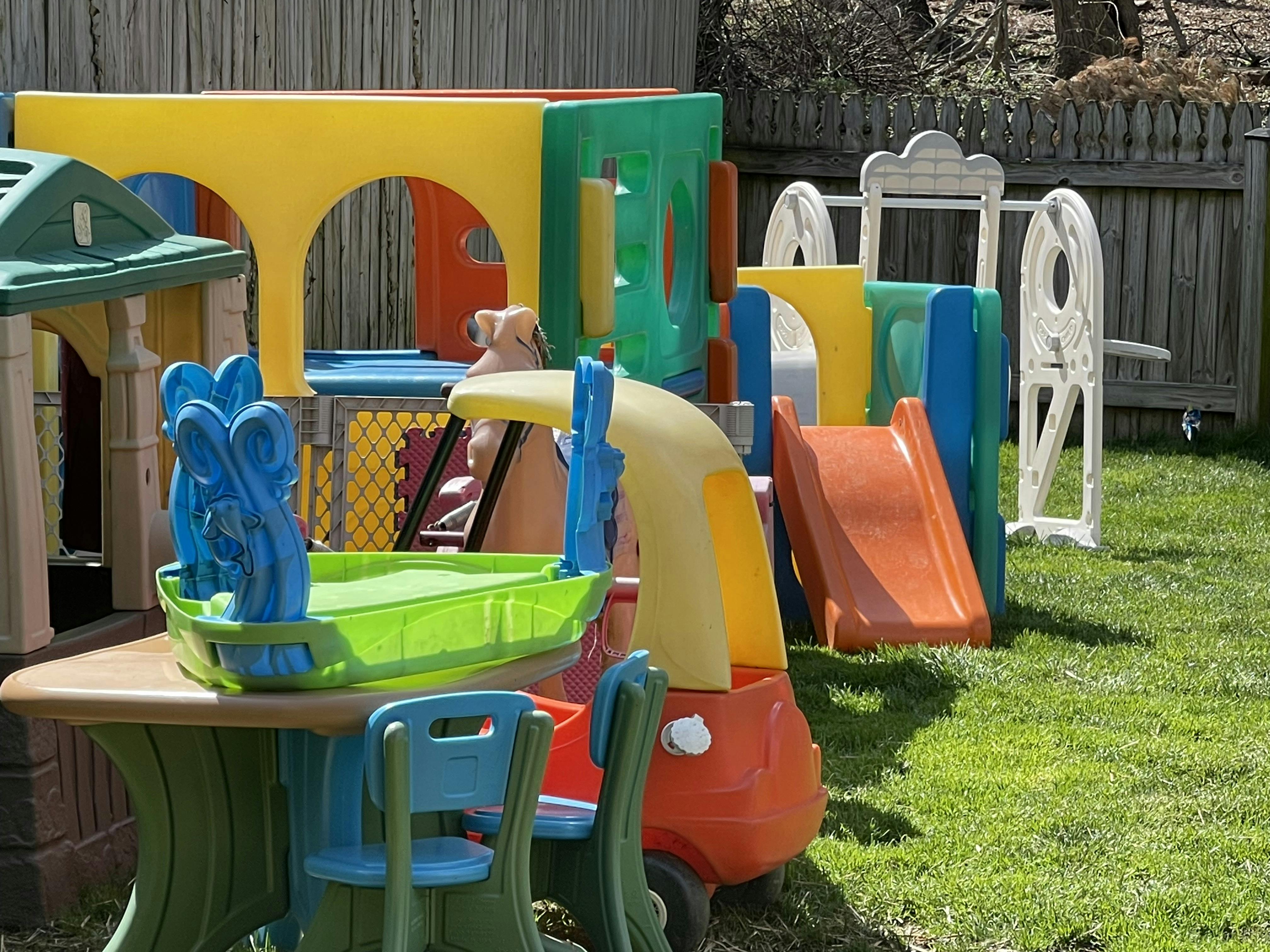 Colorful plastic children's play structures, slide, table, and chairs in a yard
