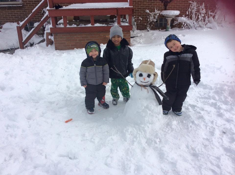 Three children standing in snow next to a snowman