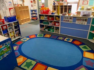 Empty classroom with a blue oval rug and shelves with toys
