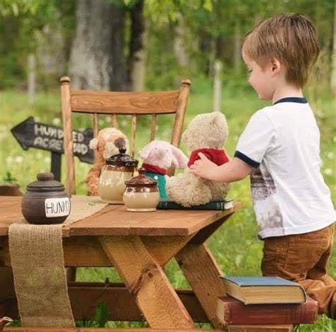 Child playing with teddy bears and honey pots on a wooden table outdoors