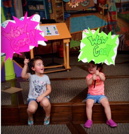 Two children holding up signs, one pink with "Just God!" and one green with "Wow God!"