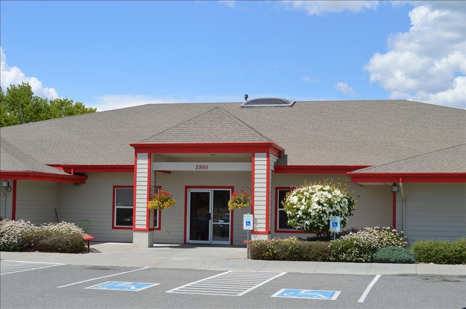 Entrance of a building with red trim, hanging flower baskets, and a parking lot