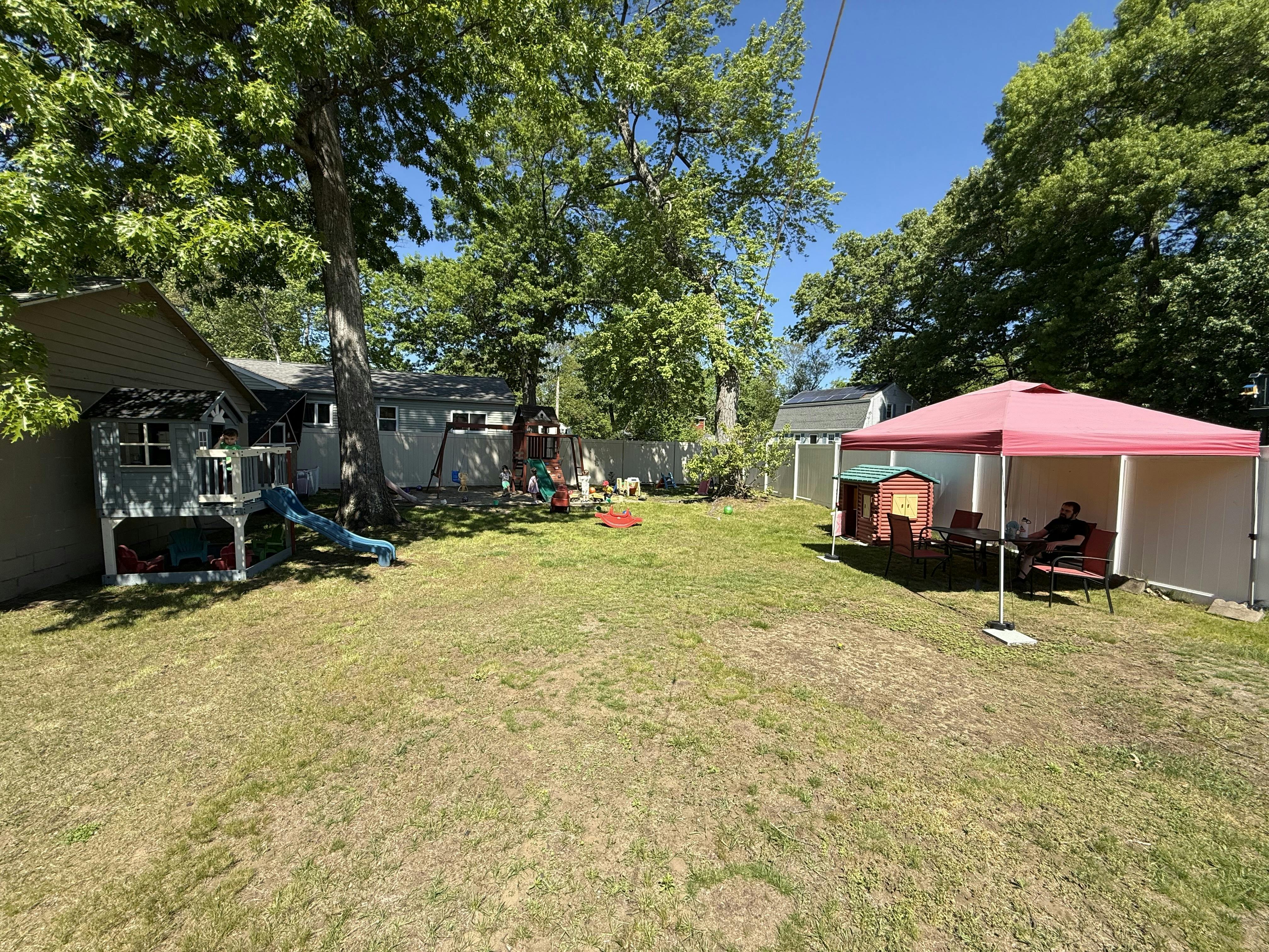 Backyard with play equipment and a canopy with a person seated underneath