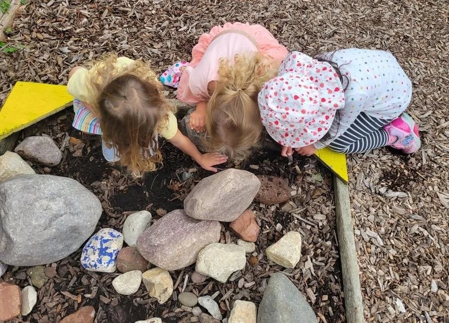 Three children looking closely at rocks and dirt on the ground
