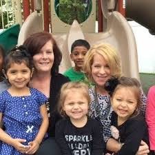 Two adults and four children smiling on a playground