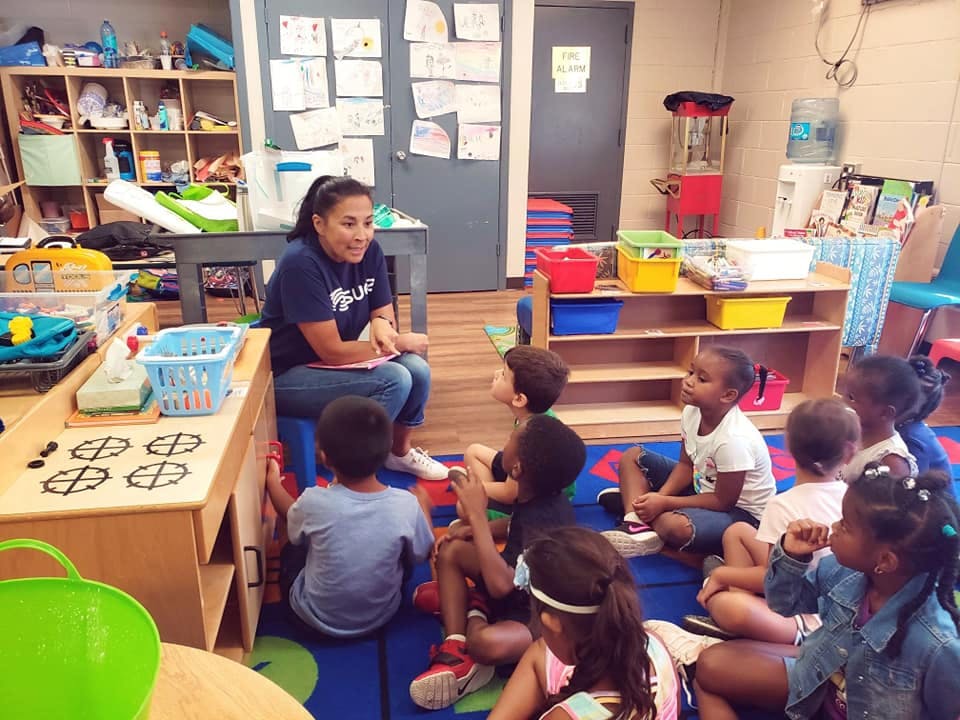 Adult person sitting on a chair with children sitting on the floor in a classroom