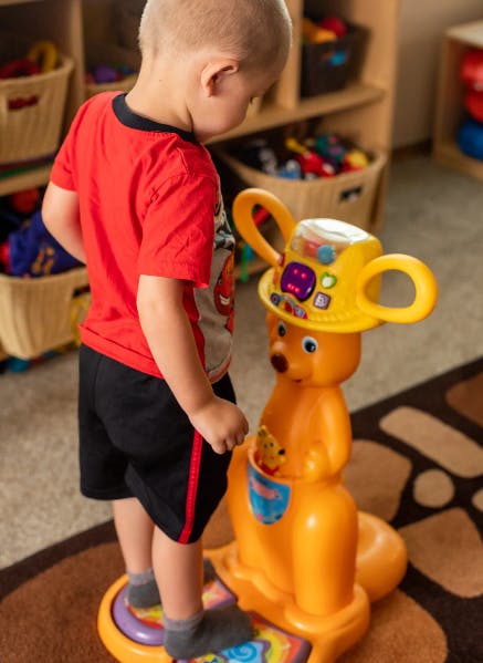 Child standing on a toy, looking at a kangaroo toy