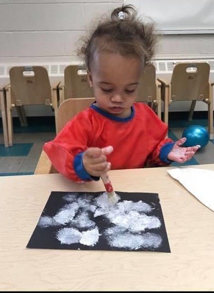 Child painting white shapes on black paper with a brush