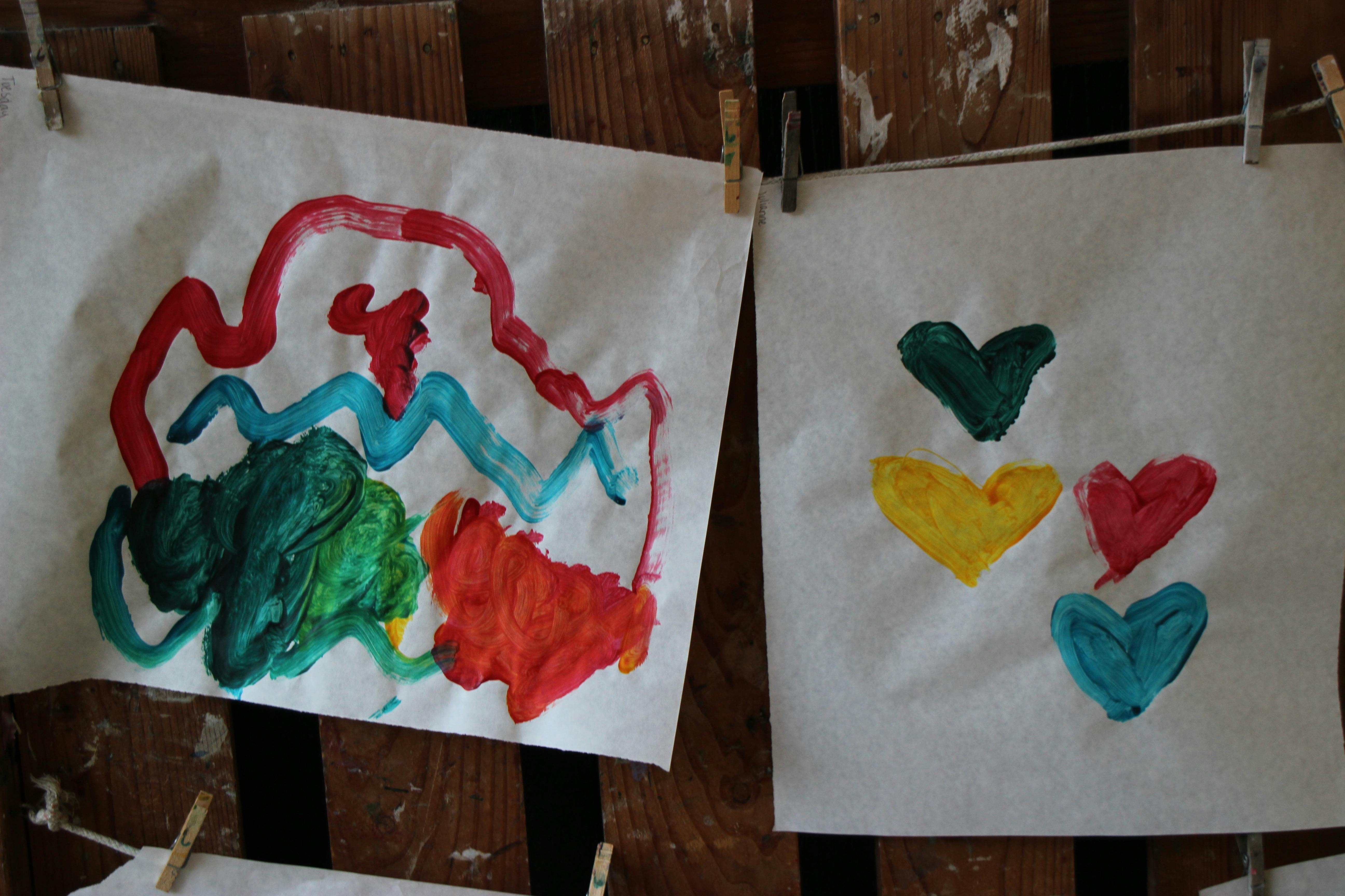 Two children's paintings hanging on a wooden wall