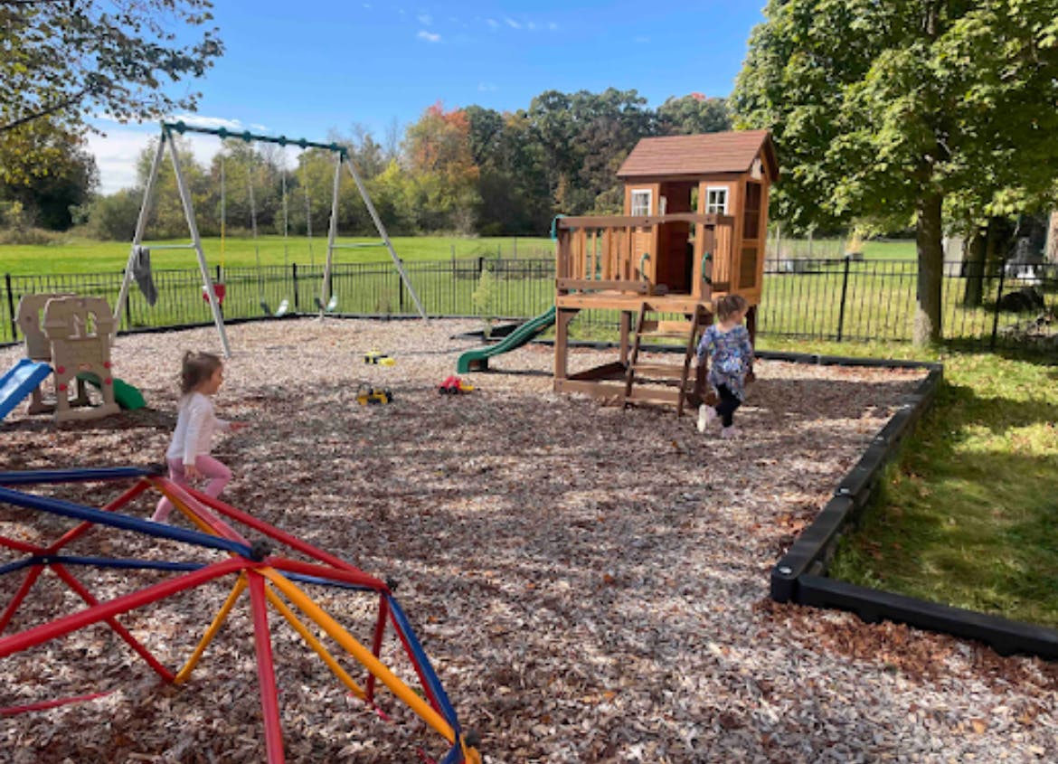 Two children playing on a playground with a swing set and playhouse