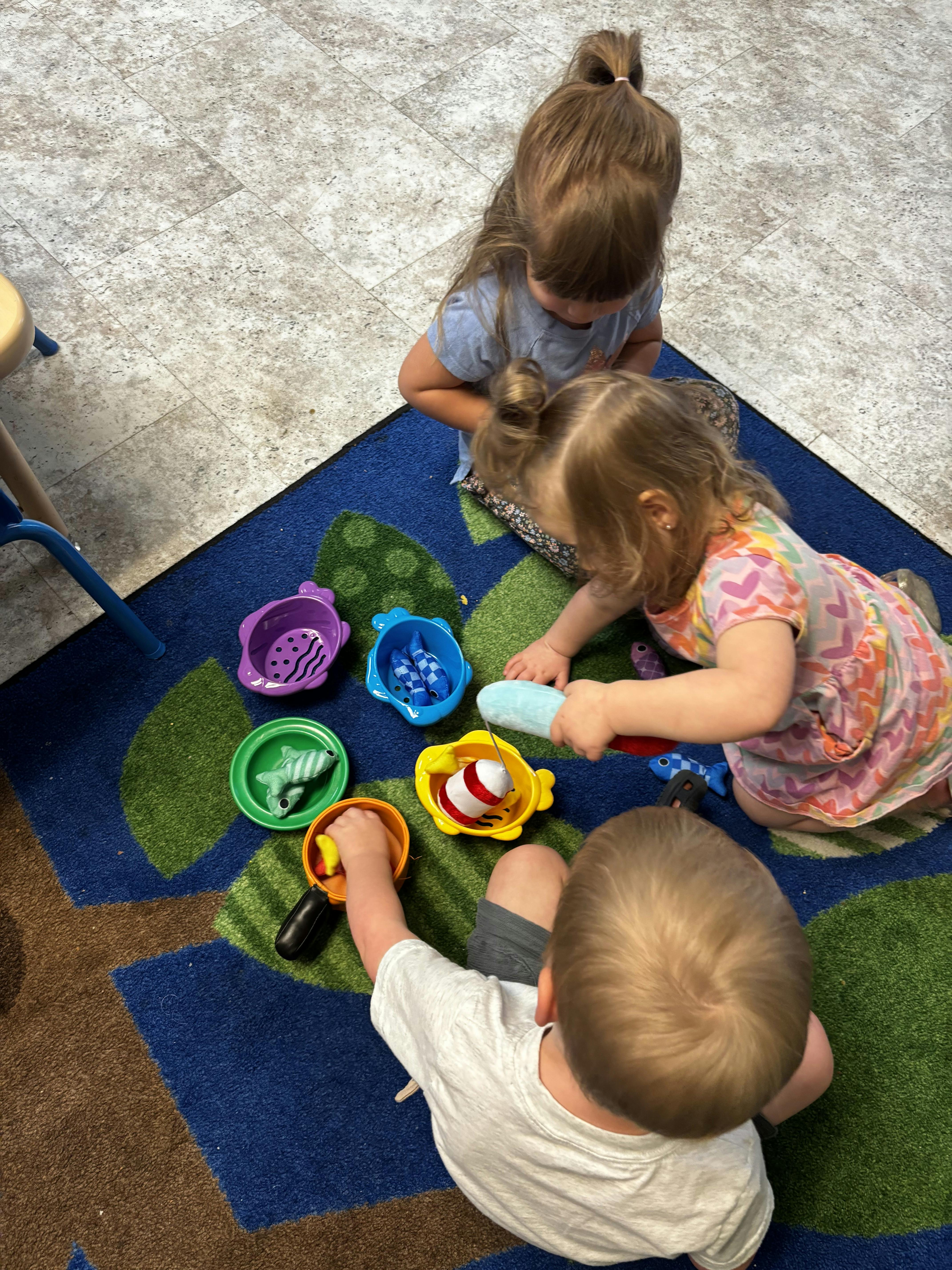 Three children playing with colorful toy fish and buckets on a patterned rug