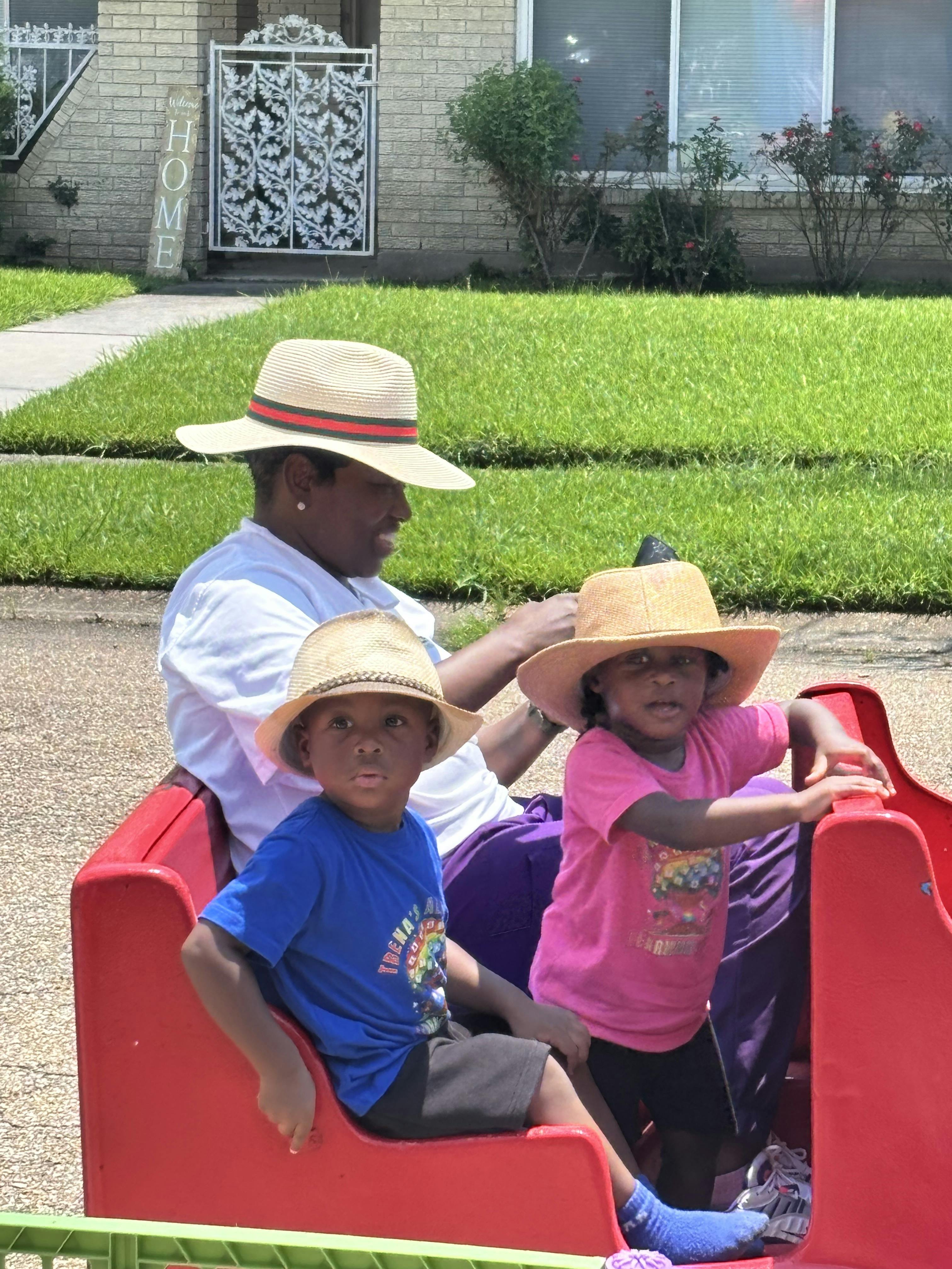 Person in a hat with two children in hats in a red wagon