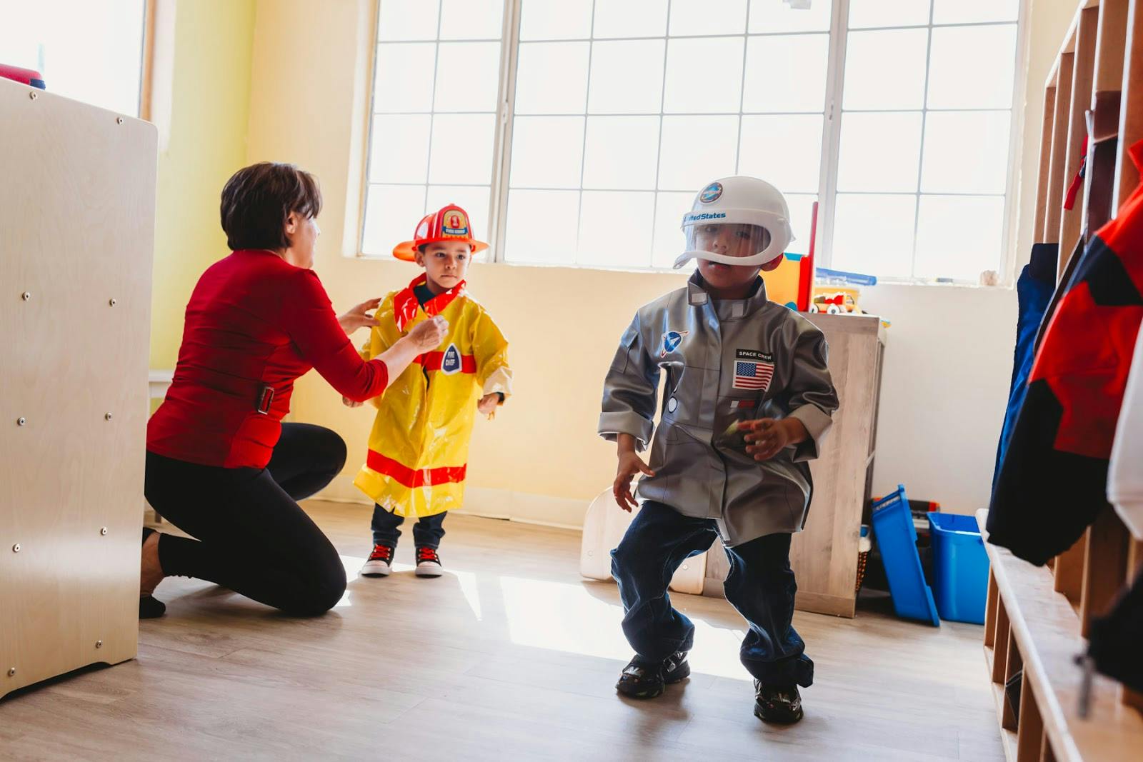Person helping child in firefighter costume, another child in astronaut costume