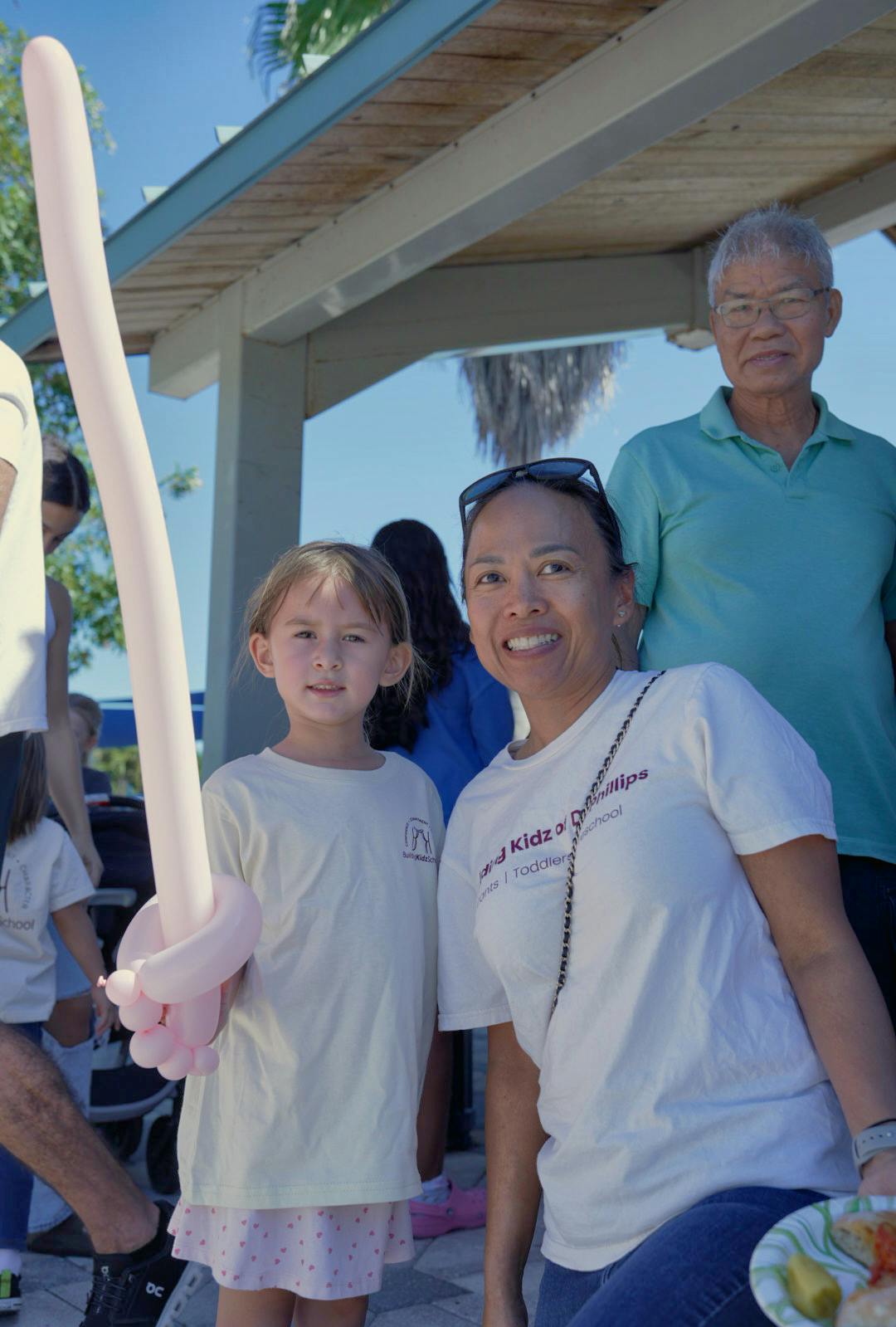 Child holding a balloon sword next to an adult outdoors