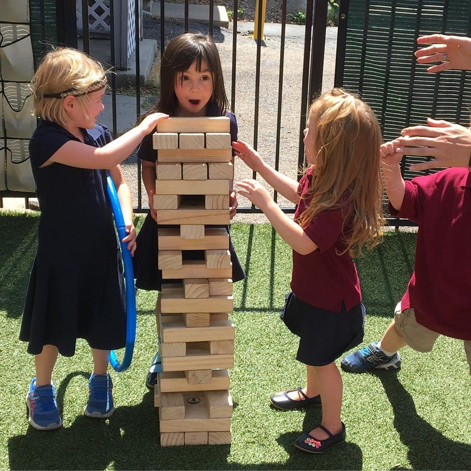 Children playing with a large wooden block tower outdoors