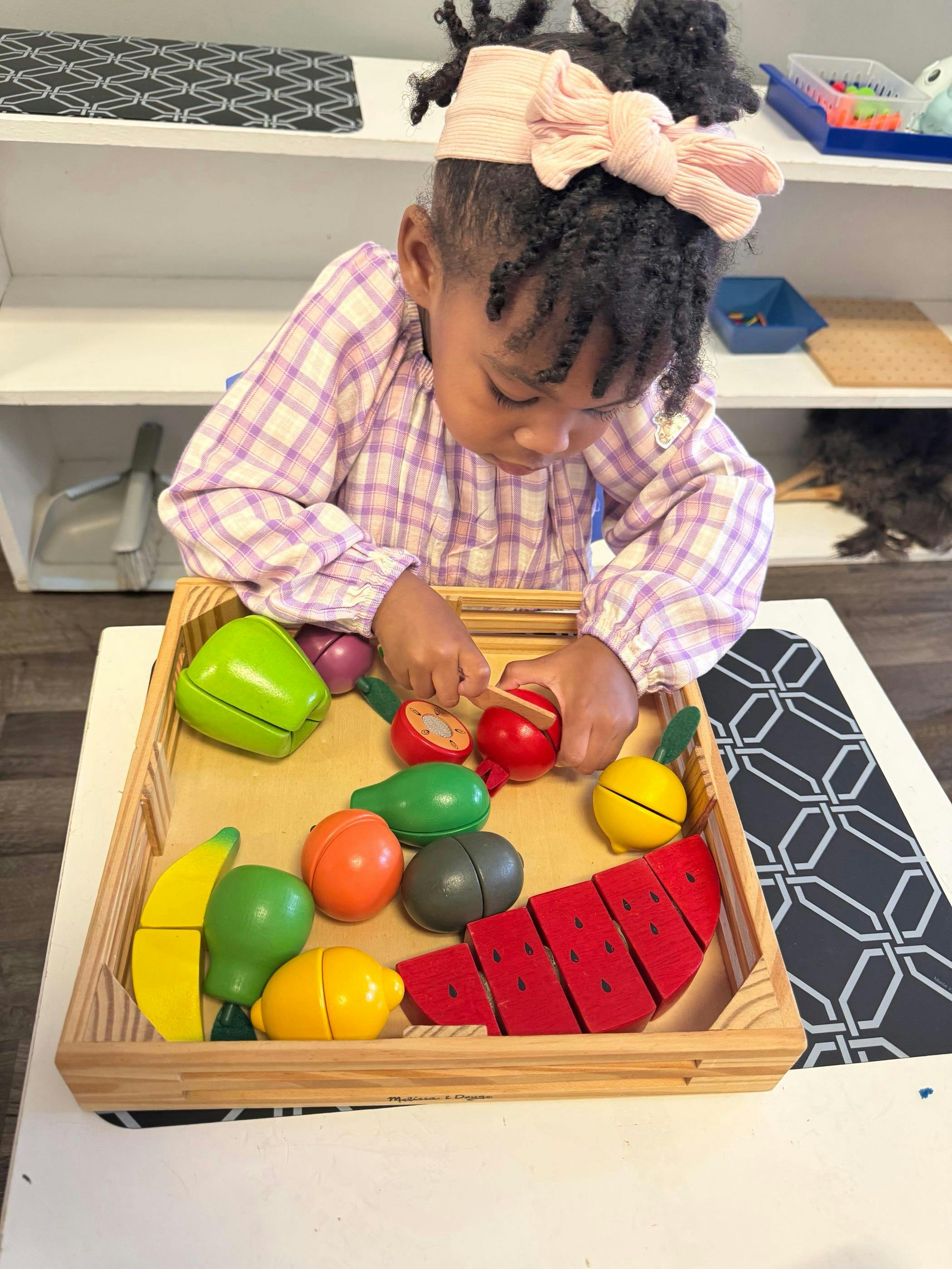 Child playing with toy fruit and knife in a wooden tray