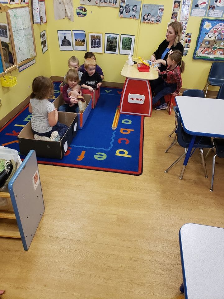Adult and children in a classroom, some children sitting in cardboard boxes