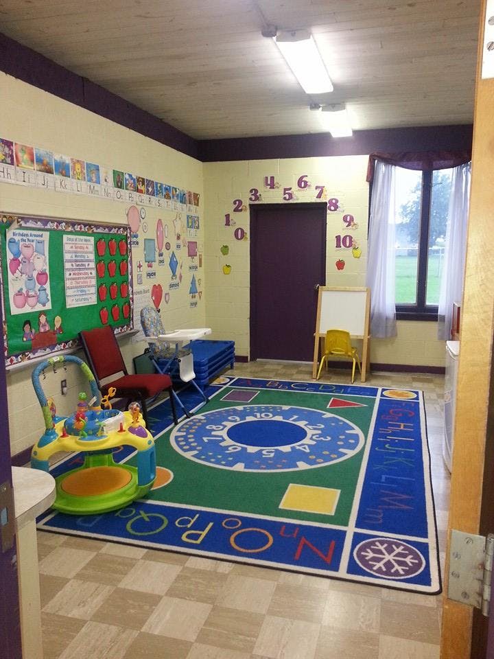 A classroom with a colorful rug, bulletin board, and child's play equipment