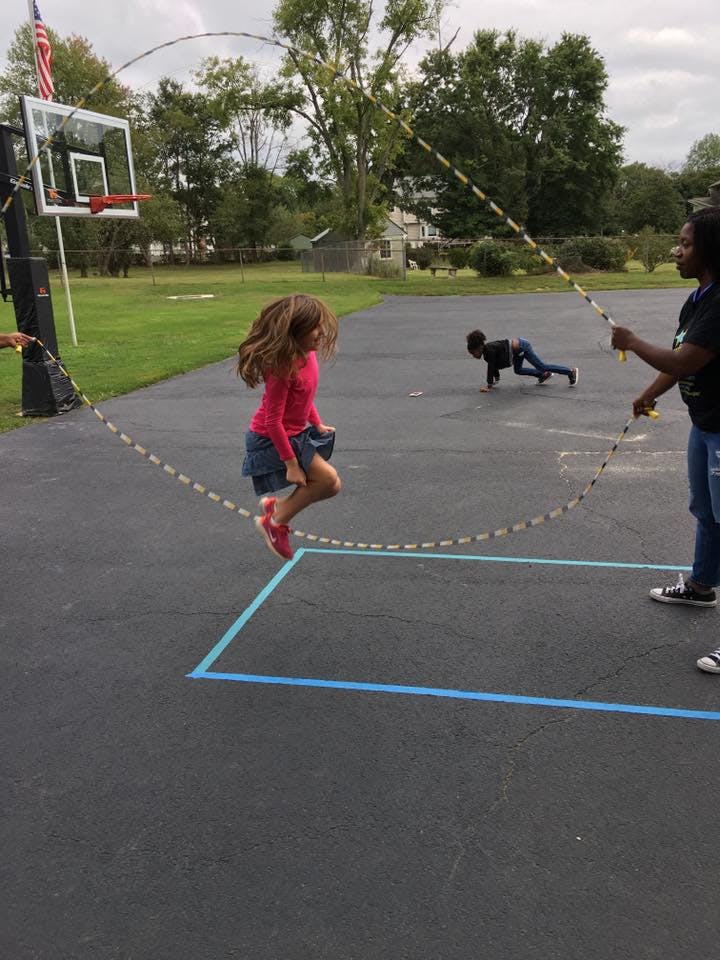 Child jumping rope while two people hold the rope