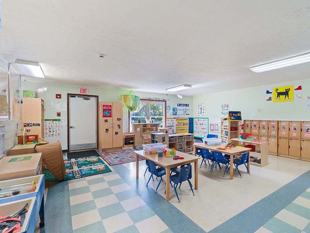 Empty children's classroom with tables, chairs, and storage